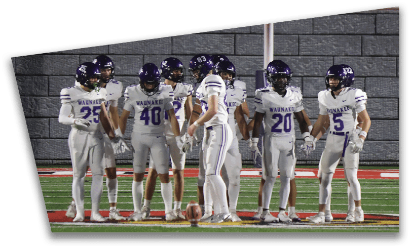 People wearing black American Canyon football uniforms and helmets are standing on a football field at night. Description generated by AI