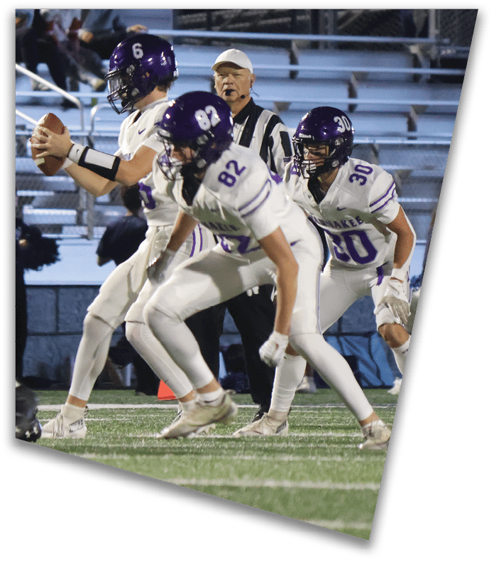 A person wearing a dark football uniform and helmet with “American Canyon" on the jersey is kneeling on one knee on a field at night. Description generated by AI