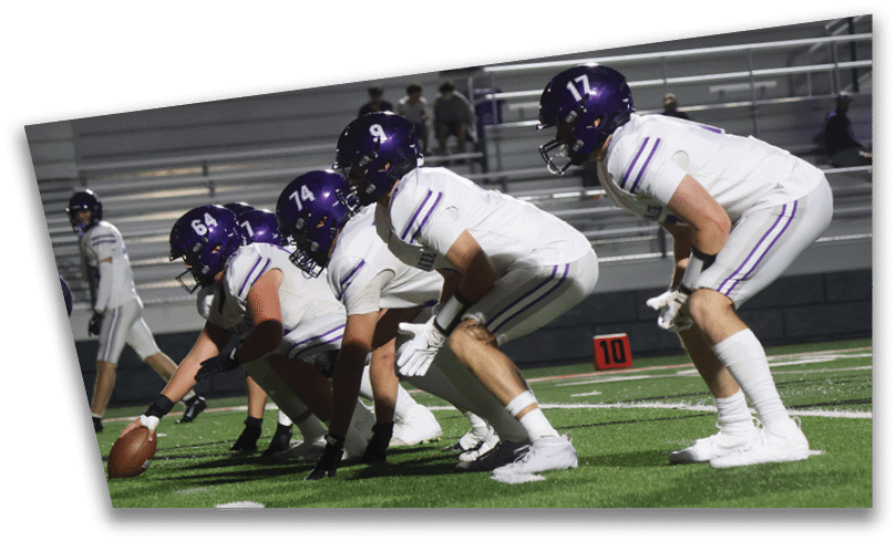 People wearing black American Canyon football uniforms and helmets are standing on a football field at night. Description generated by AI