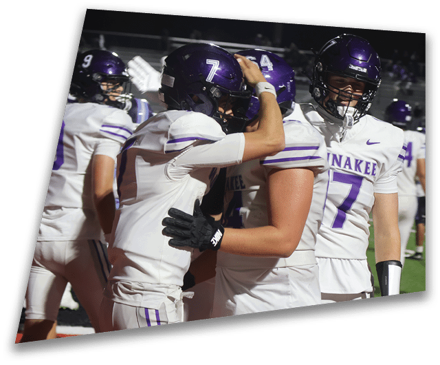 Four people in dark football uniforms and helmets stand in a row on a field, appearing focused and ready for action. Description generated by AI