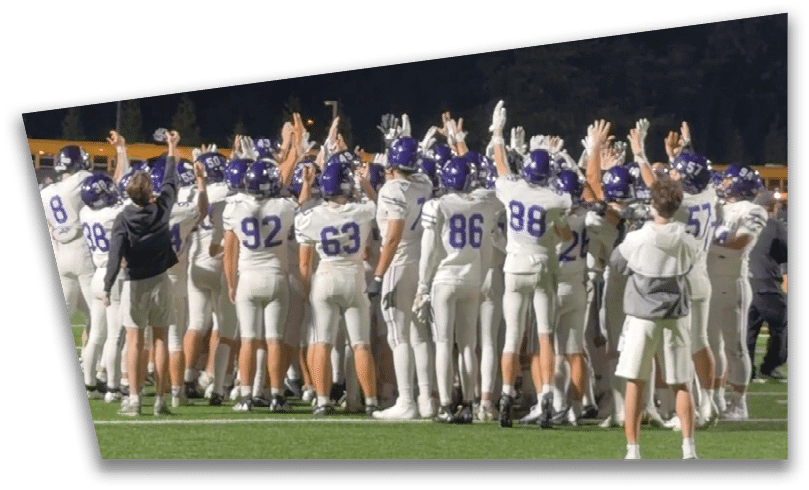 People wearing black American Canyon football uniforms and helmets are standing on a football field at night. Description generated by AI