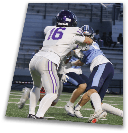 A person in a black football uniform and helmet is crouched in a ready position on a green field with another player in white uniform visible in the background. Description generated by AI
