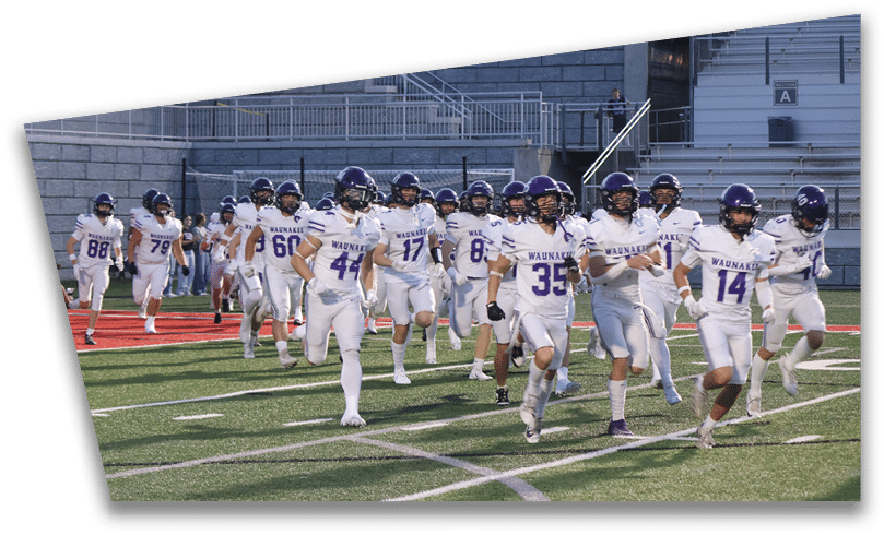 People wearing black American Canyon football uniforms and helmets are standing on a football field at night. Description generated by AI