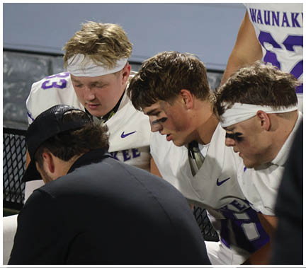 A group of football players huddled together on the field. Description generated by AI