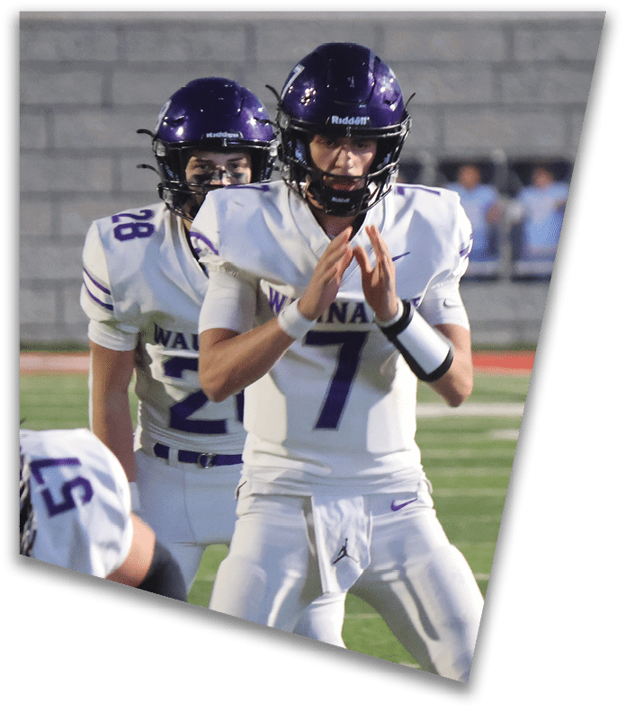 A person wearing a dark football uniform and helmet with “American Canyon" on the jersey is kneeling on one knee on a field at night. Description generated by AI