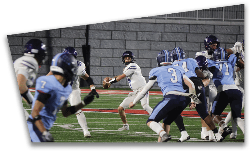 People wearing black American Canyon football uniforms and helmets are standing on a football field at night. Description generated by AI