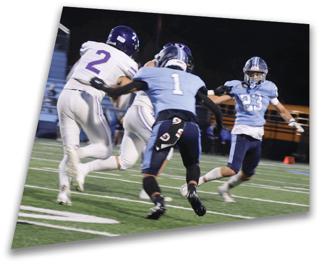Four people in dark football uniforms and helmets stand in a row on a field, appearing focused and ready for action. Description generated by AI