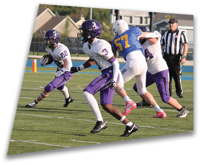 Four people in dark football uniforms and helmets stand in a row on a field, appearing focused and ready for action. Description generated by AI