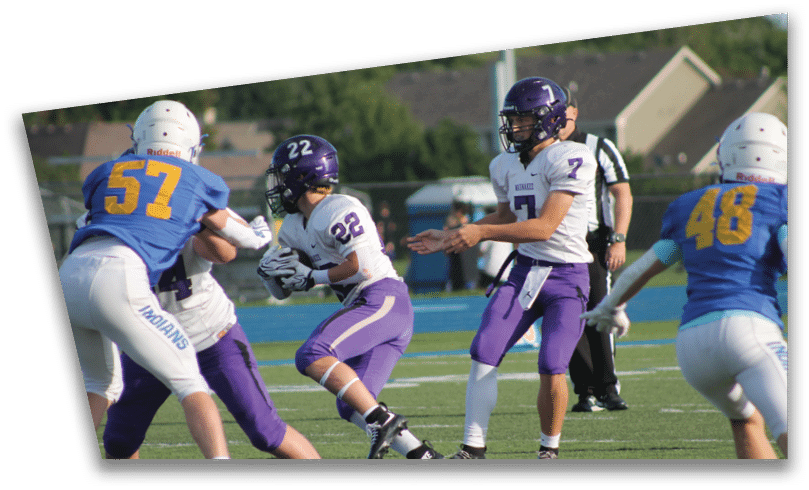 People wearing black American Canyon football uniforms and helmets are standing on a football field at night. Description generated by AI