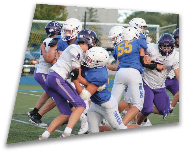 Four people in dark football uniforms and helmets stand in a row on a field, appearing focused and ready for action. Description generated by AI