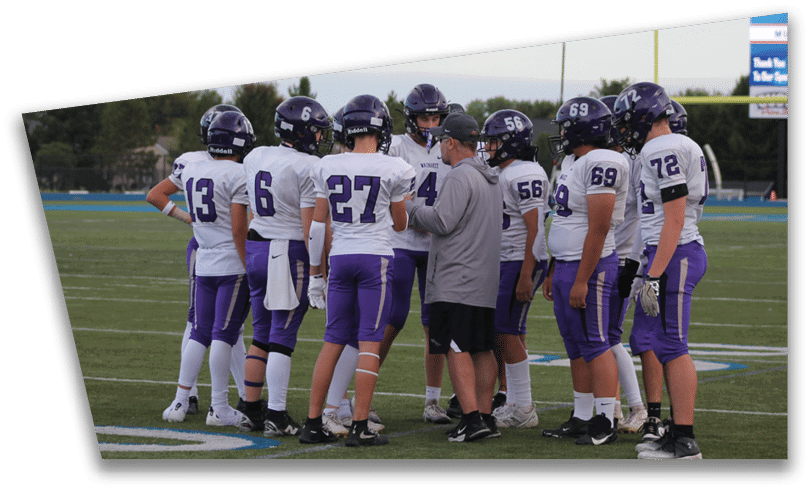 People wearing black American Canyon football uniforms and helmets are standing on a football field at night. Description generated by AI