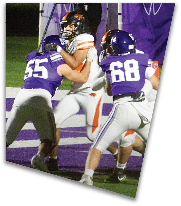 A person wearing a dark football uniform and helmet with “American Canyon" on the jersey is kneeling on one knee on a field at night. Description generated by AI