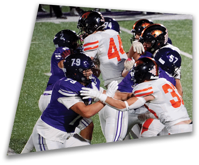Four people in dark football uniforms and helmets stand in a row on a field, appearing focused and ready for action. Description generated by AI