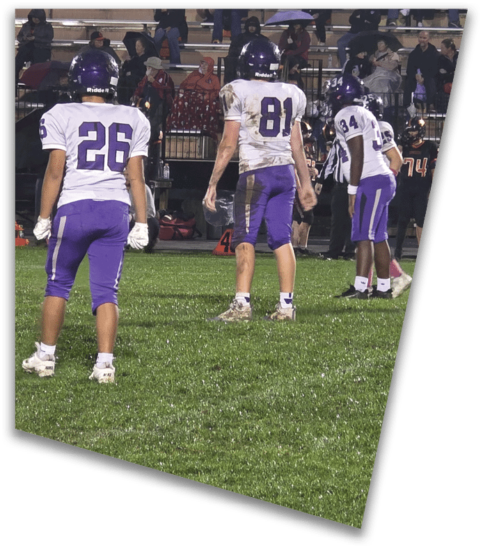 A person wearing a dark football uniform and helmet with “American Canyon" on the jersey is kneeling on one knee on a field at night. Description generated by AI