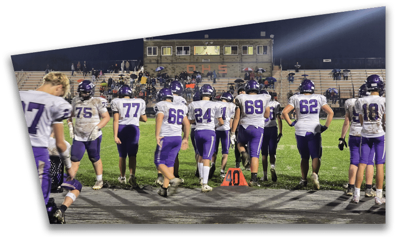 People wearing black American Canyon football uniforms and helmets are standing on a football field at night. Description generated by AI