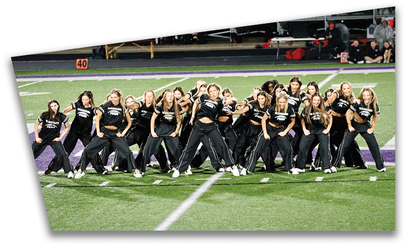People wearing black American Canyon football uniforms and helmets are standing on a football field at night. Description generated by AI