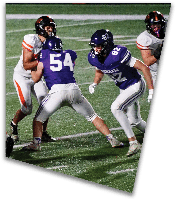 A person wearing a dark football uniform and helmet with “American Canyon" on the jersey is kneeling on one knee on a field at night. Description generated by AI