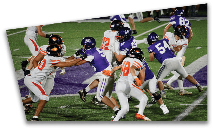 People wearing black American Canyon football uniforms and helmets are standing on a football field at night. Description generated by AI