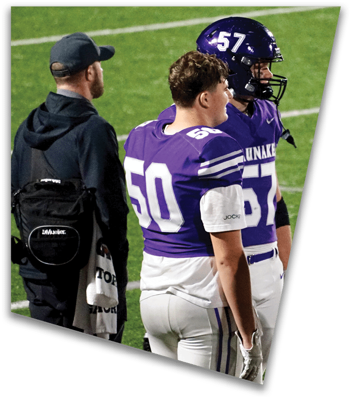 A person wearing a dark football uniform and helmet with “American Canyon" on the jersey is kneeling on one knee on a field at night. Description generated by AI