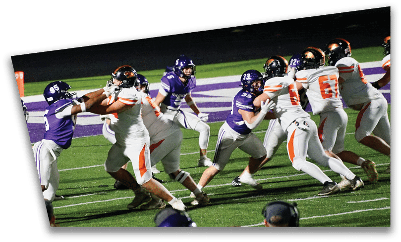 People wearing black American Canyon football uniforms and helmets are standing on a football field at night. Description generated by AI