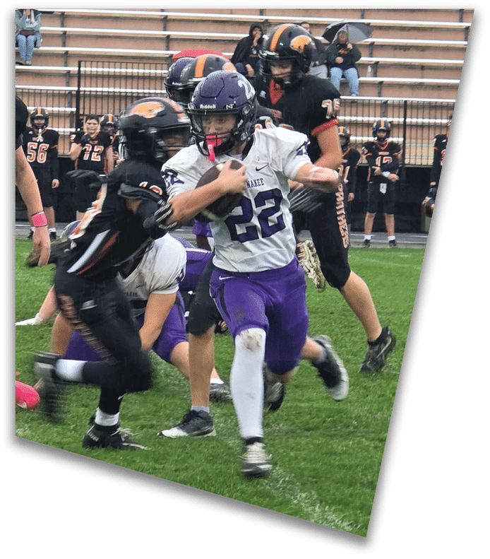 A person wearing a dark football uniform and helmet with “American Canyon" on the jersey is kneeling on one knee on a field at night. Description generated by AI