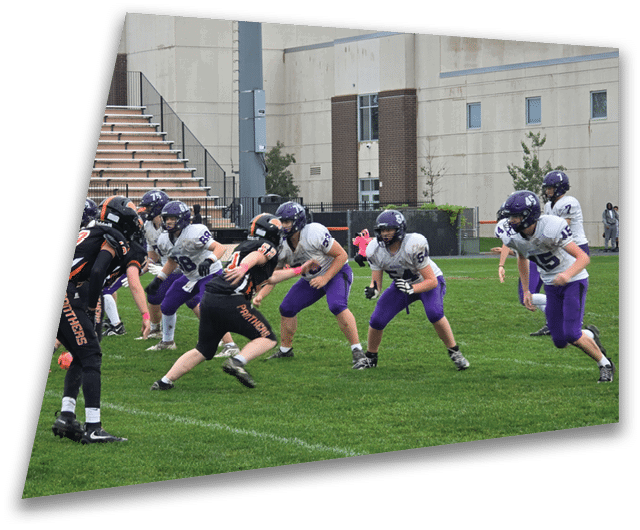 Four people in dark football uniforms and helmets stand in a row on a field, appearing focused and ready for action. Description generated by AI