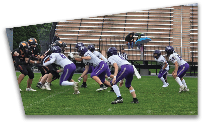 People wearing black American Canyon football uniforms and helmets are standing on a football field at night. Description generated by AI