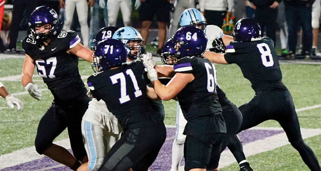 Four people wearing black football uniforms with “VISTA" on the front are standing together in a stadium with a crowd in the background, two of them holding helmets raised above their heads. Description generated by AI