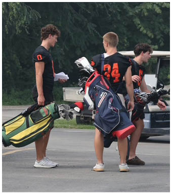 Three people wearing casual clothing and sneakers are standing near a golf cart on a paved surface. Description generated by AI