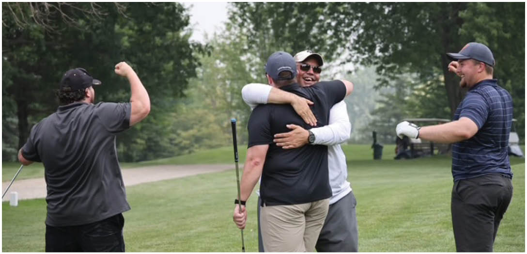 Four adults on a golf course are celebrating with one hugging another while the others cheer and smile. Description generated by AI