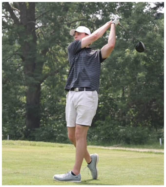 A person wearing a striped shirt, light shorts, and a white cap is swinging a golf club on a grassy area with trees in the background. Description generated by AI