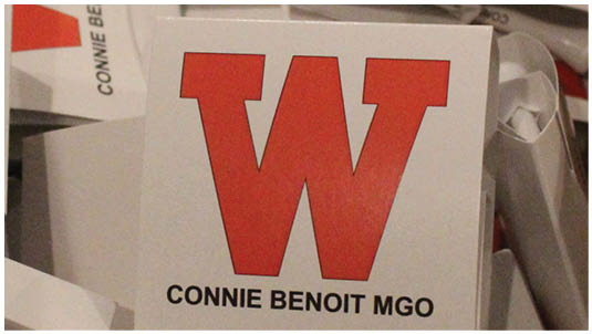 A close-up of a white card with a large red letter W and the text “CONNIE BENOIT MGO" below it. Description generated by AI