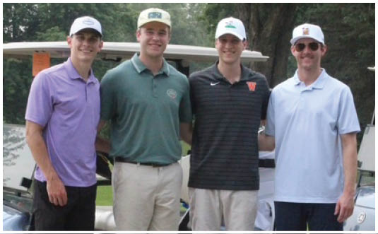 Four adults wearing casual golf attire stand together smiling in front of two golf carts on a paved path with grass and trees in the background. Description generated by AI