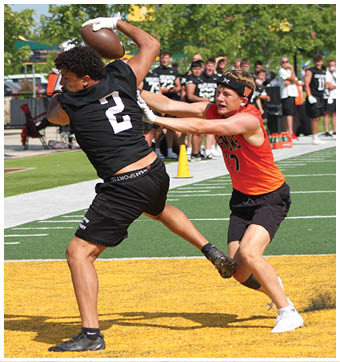 An adult wearing an orange sleeveless shirt and black shorts is actively reaching out to block or tag another person dressed in black athletic clothing on a sports field. Description generated by AI