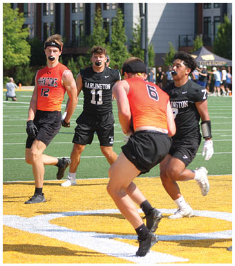 People wearing sports uniforms and mouthguards are actively playing a game on a field with artificial turf and a yellow end zone. Description generated by AI