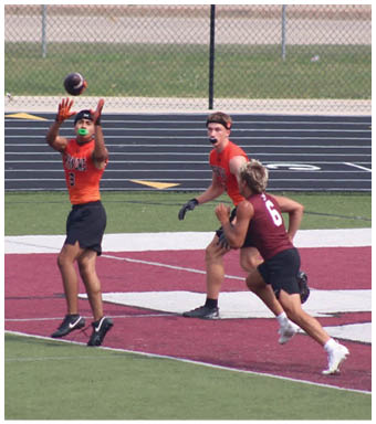 Three people wearing sports uniforms are playing football on a field with one person jumping to catch the ball while the others run nearby. Description generated by AI