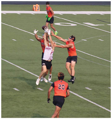 People wearing athletic clothing are jumping and reaching to catch a football on a sports field marked with yard lines. Description generated by AI