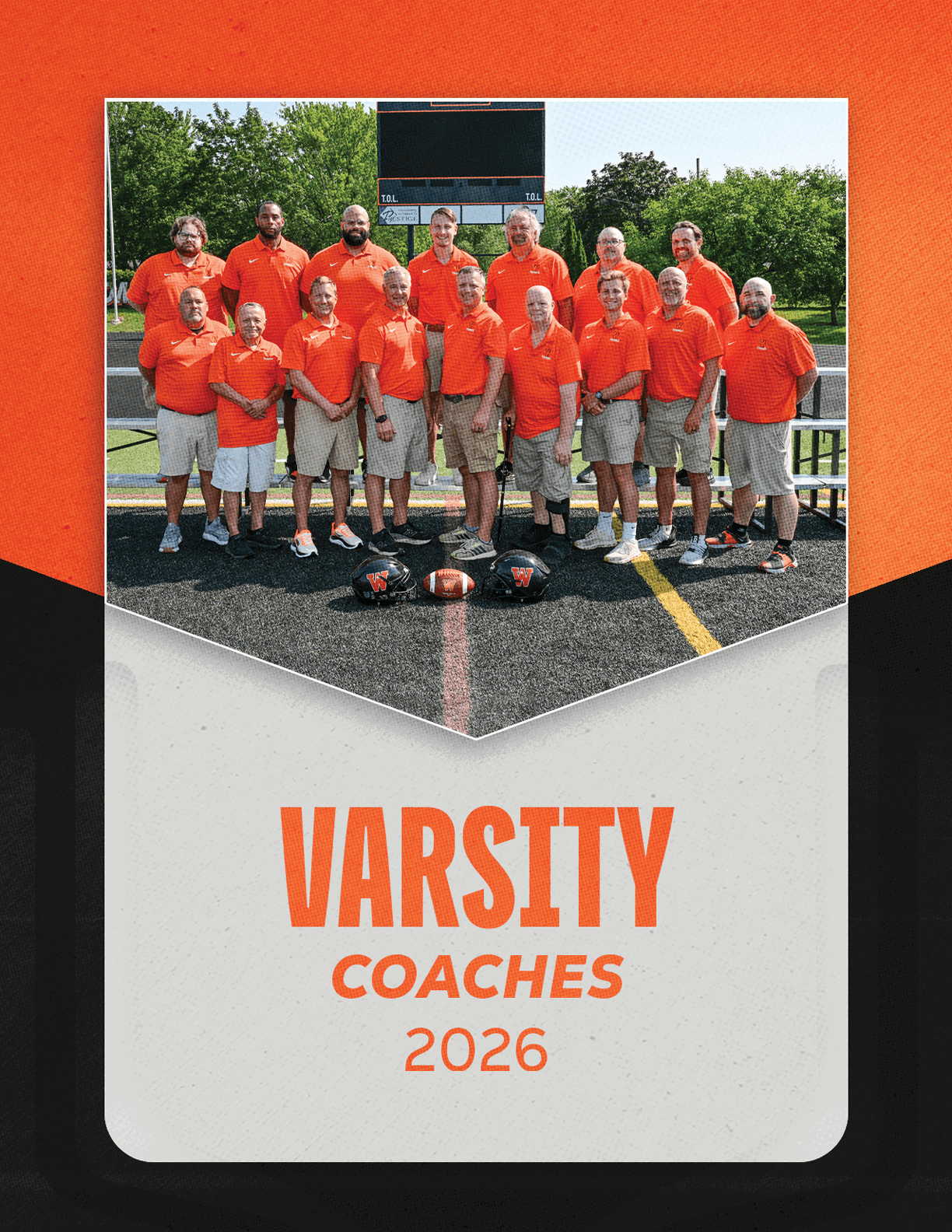 A group of adults wearing matching orange shirts and khaki shorts pose together on a sports field with football helmets and a football in front of them, above the text “VARSITY COACHES 2026." Description generated by AI