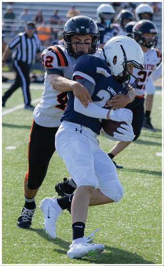 Two people in football uniforms are engaged in a tackle on a grassy field during a game. Description generated by AI
