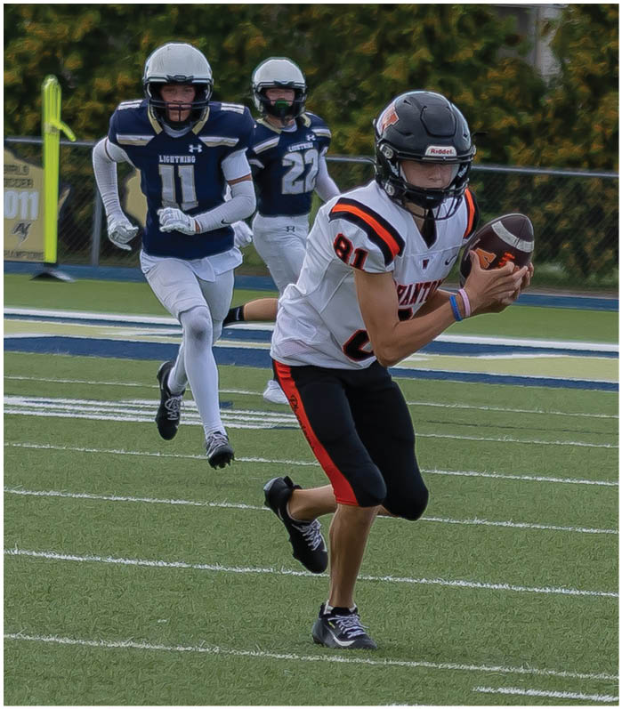 A person in a black and orange football uniform is holding a football and running on a field while two people in blue and white uniforms chase behind. Description generated by AI