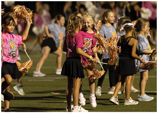 People wearing cheerleading outfits hold orange and white pom-poms while standing on a field. Description generated by AI