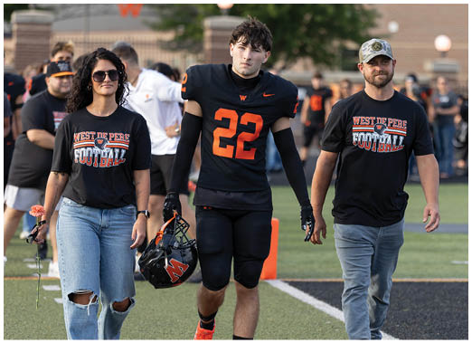 A person wearing a black football uniform with the number 22 and another person in a black West De Pere Football t-shirt are walking side by side on a sports field. Description generated by AI
