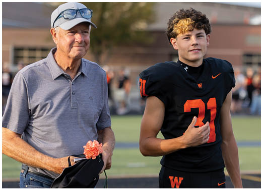 A person wearing a black football jersey with the number 31 in orange is giving a thumbs-up gesture on a sports field. Description generated by AI