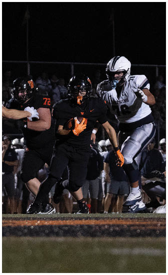 Two football players in white and black uniforms are engaged in a play on a field at night with spectators in the background. Description generated by AI