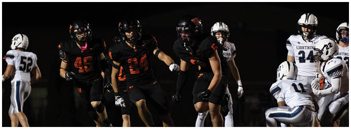 People wearing football uniforms are engaged in a game on a field at night. Description generated by AI