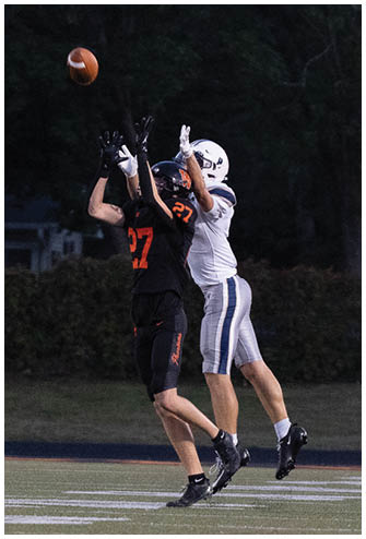 A person wearing a black football uniform with the number 31 is kicking a football on a field with trees and a building in the background. Description generated by AI