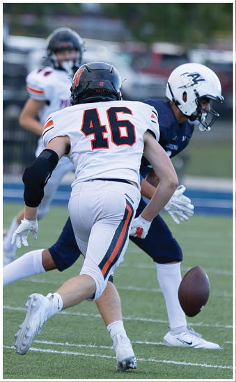 Two people in football uniforms are engaged in a play on a field with one person wearing a white jersey with the number 46 and the other in a dark uniform. Description generated by AI
