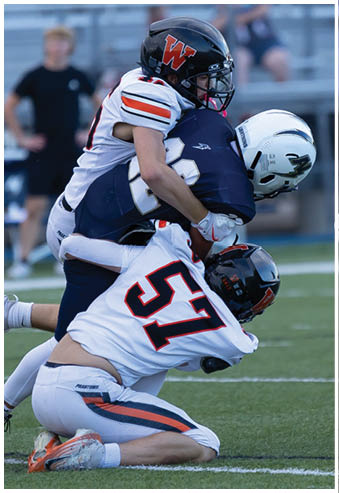 Two people in football uniforms are engaged in a tackle on a field with one player wearing a helmet marked with a “W" and the other player grabbing onto them. Description generated by AI