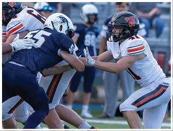 People in football uniforms are engaged in a close physical play on the field during a game. Description generated by AI