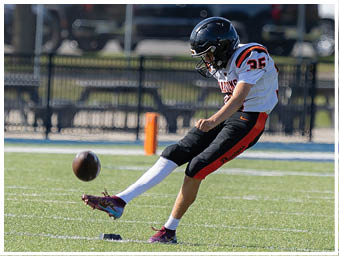 A person wearing a football uniform is kicking a football on a grassy field near an orange marker. Description generated by AI